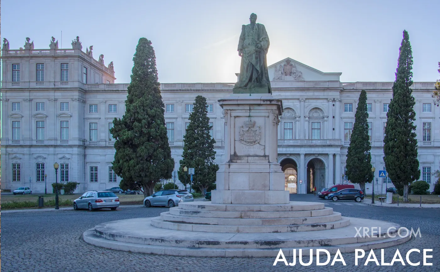 Palácio Nacional da Ajuda ao anoitecer. A fachada neoclássica domina a praça no alto da colina, com a estátua real de sentinela.